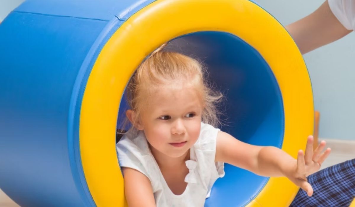 A child crawling through a padded therapy tunnel with a therapist's support